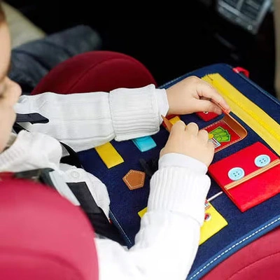 Child playing with interactive fabric activity book in a car seat.