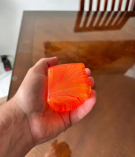 A hand holding a bright orange bar of soap with a red swirl pattern.