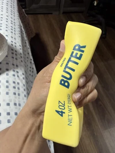 A hand squeezing a yellow, butter-shaped stress toy that says 'SALTED BUTTER' on the side.