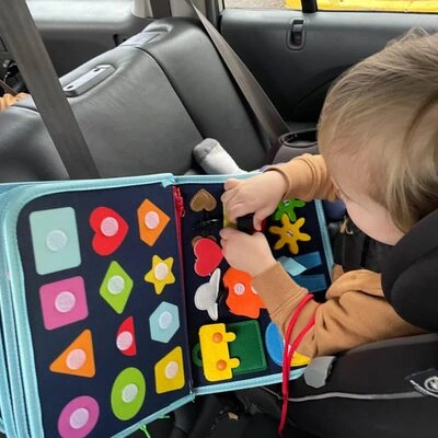 Child playing with a colorful activity book in a car seat.