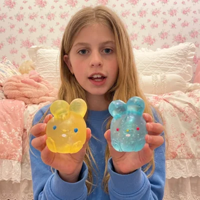 A young girl with blonde hair holds up a yellow and a blue bunny-shaped toy.