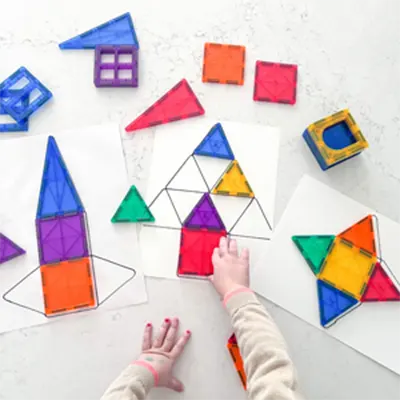 Child arranging colorful geometric tiles on paper outlines.