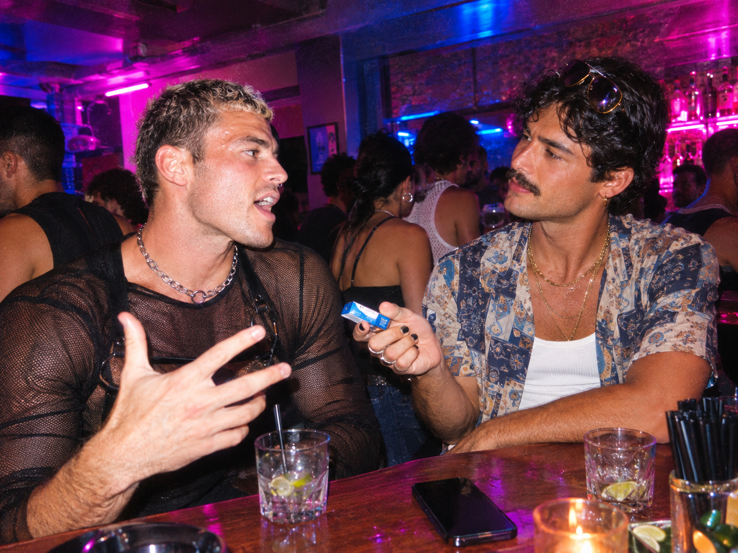 Two men at a bar, one quietly offering the other a pack of gum