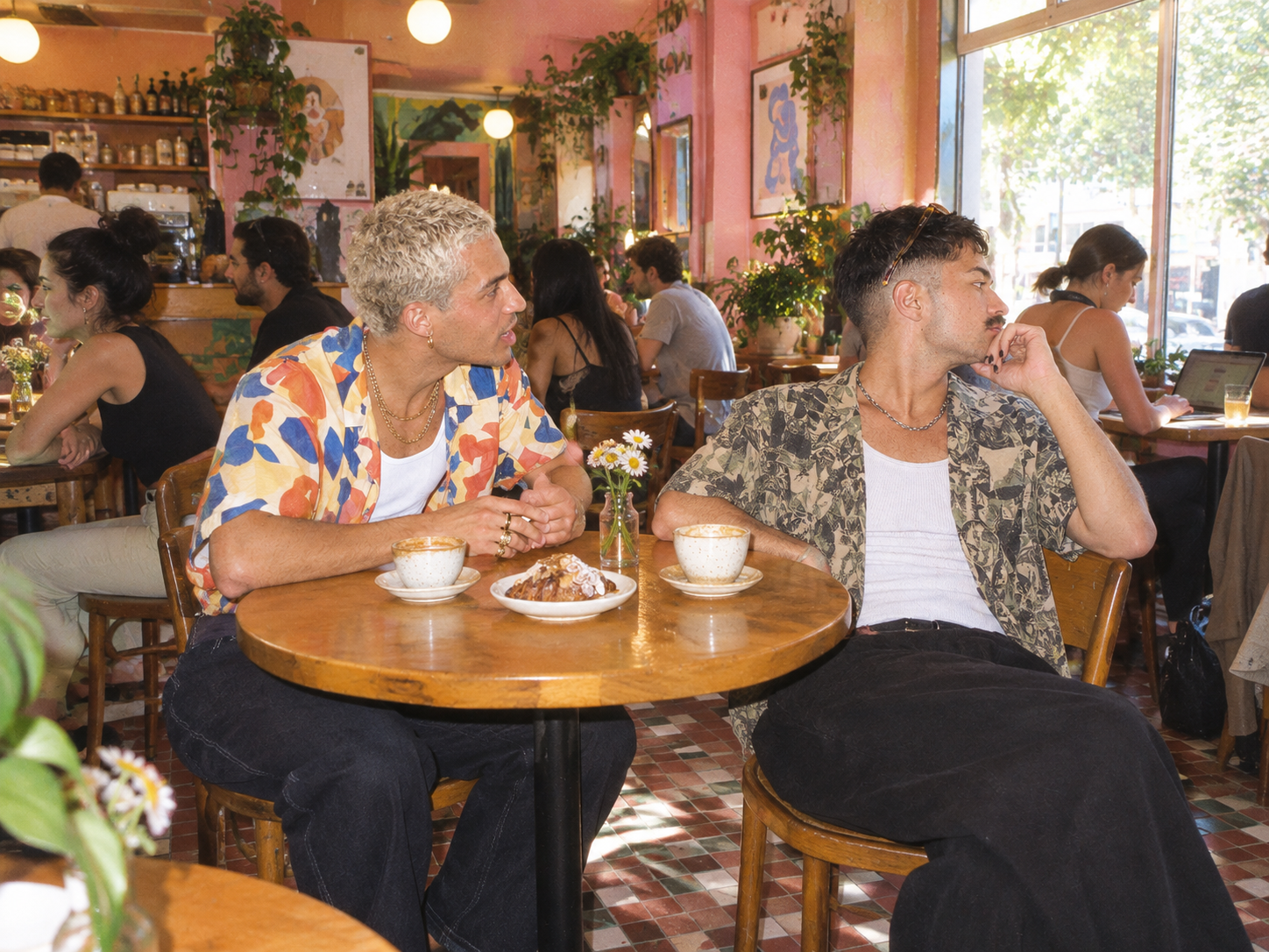 Two men at a cafe table, one leaning in while the other looks away
