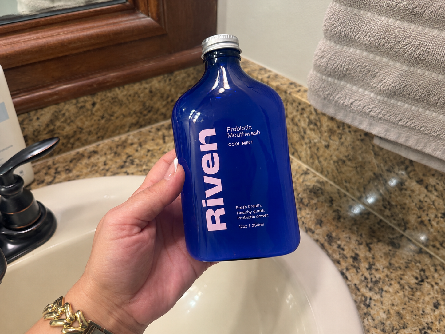A hand holding a bottle of Riven probiotic mouthwash over the bathroom sink