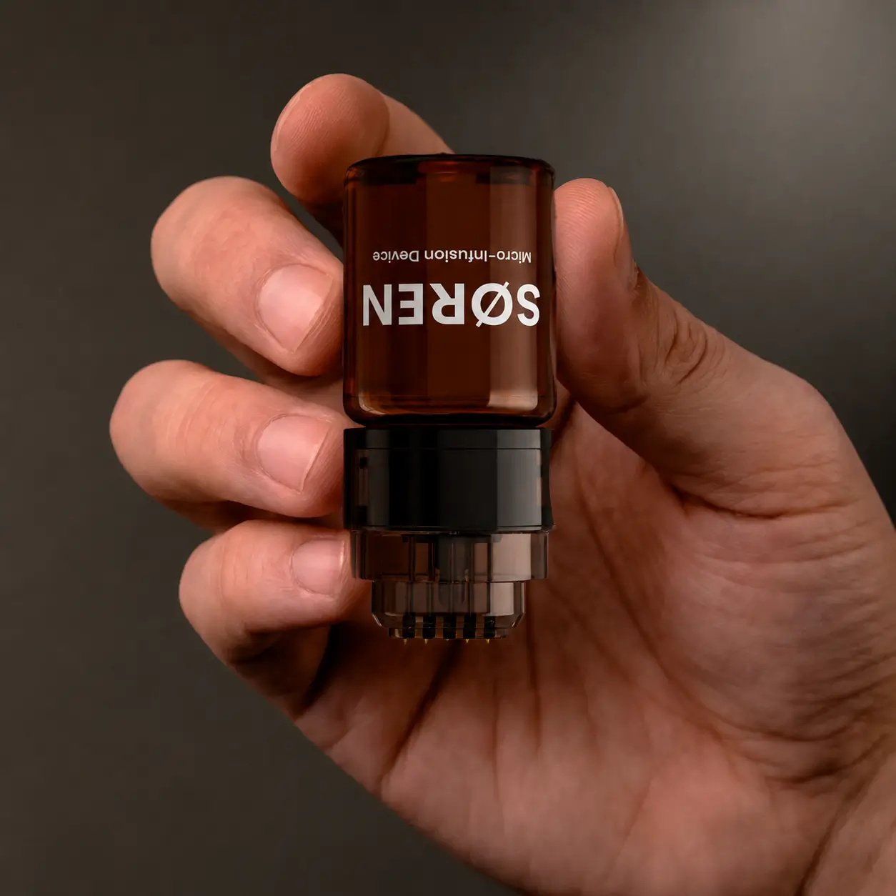 Hand holding the assembled SØREN micro-infusion device upside down.