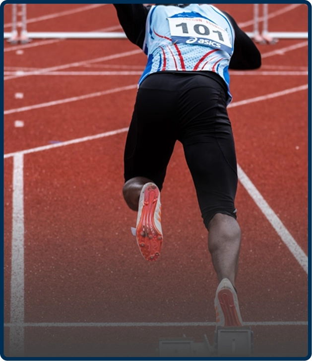 Athlete running on a red track, wearing a numbered jersey and spikes.