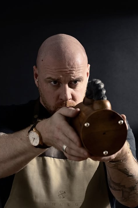 Bald man aiming a wooden object with a focused expression.