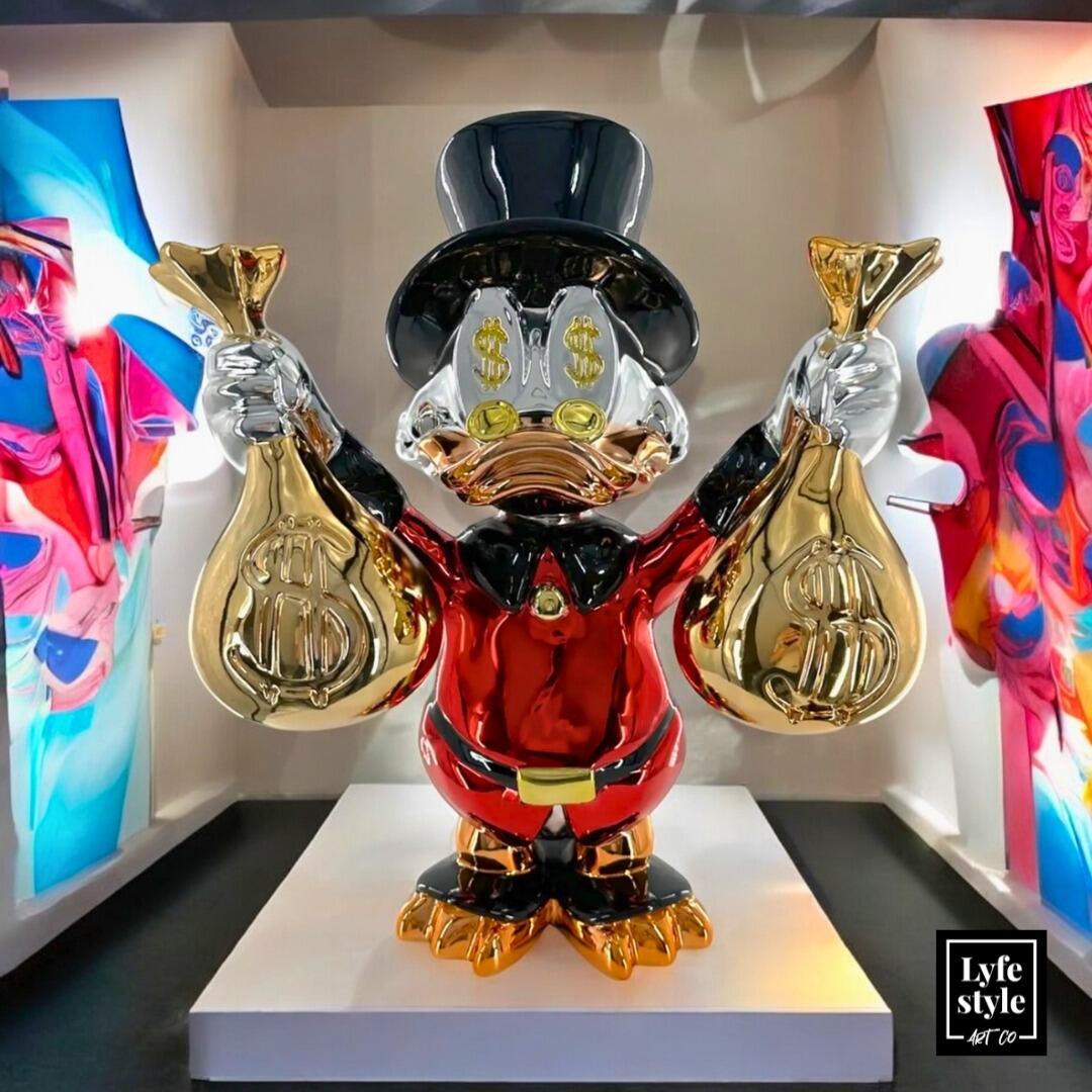 A duck figurine in a suit and hat holding two gold money bags with dollar signs.