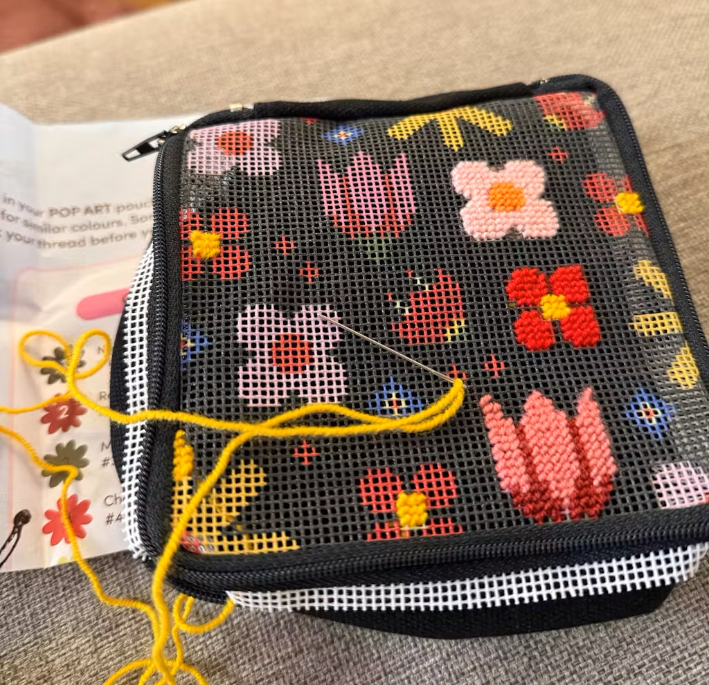 Embroidery project with needle and yellow thread on floral mesh fabric.