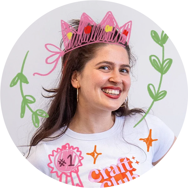 Smiling person wearing a white 'craft club' t-shirt with colorful doodles, including a crown and plants.
