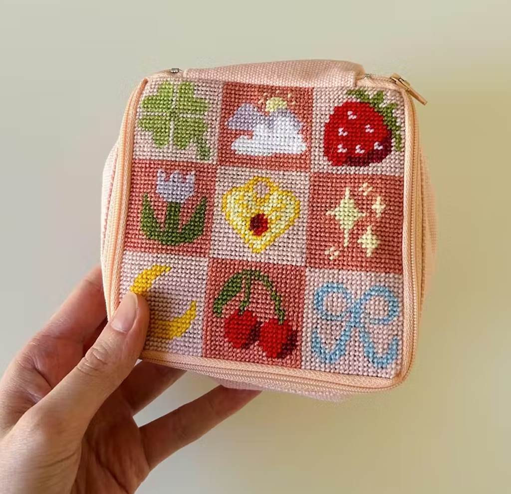 Hand holding pink pouch with stitched symbols like clover, strawberry, and moon.