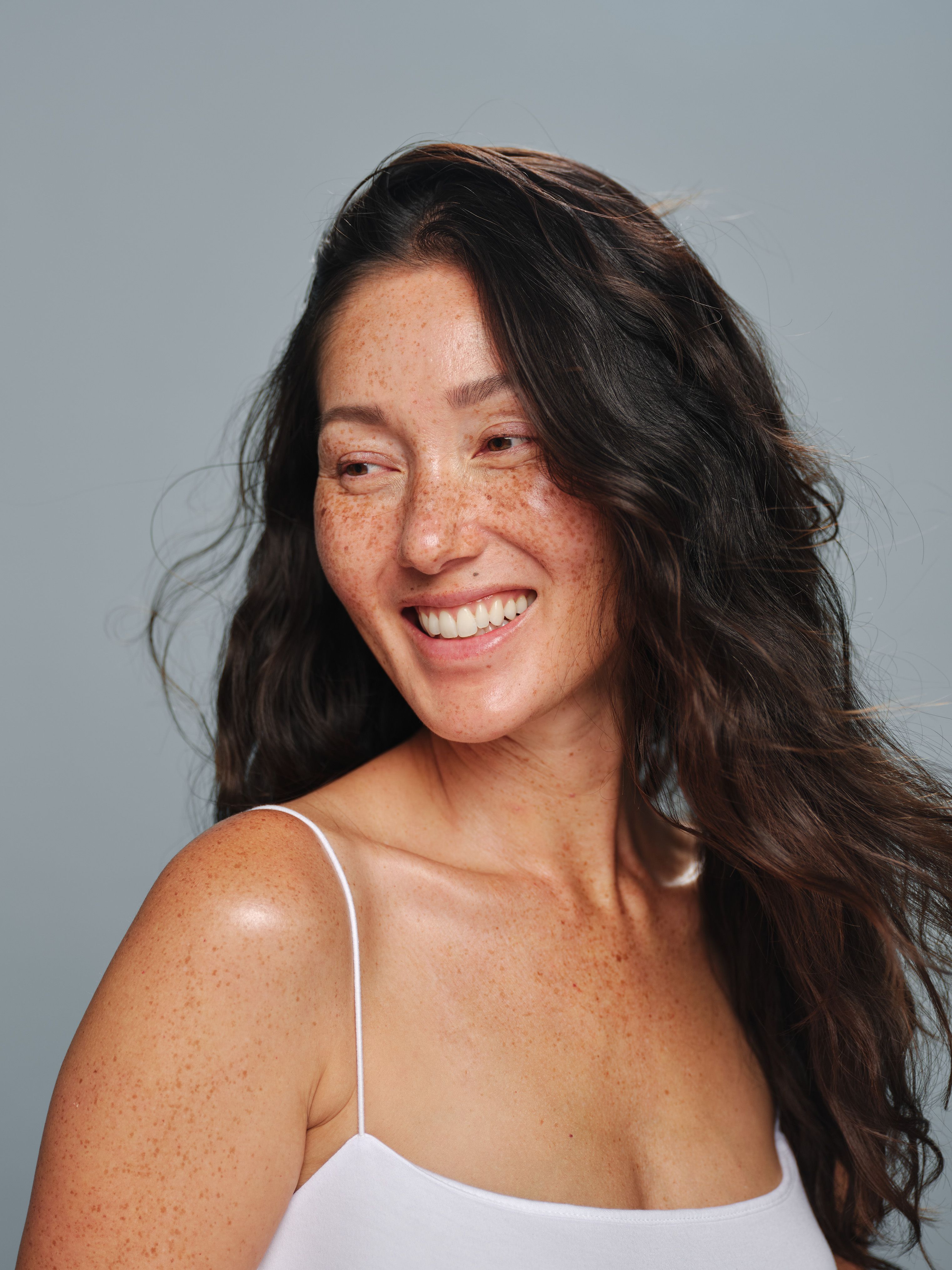 Smiling person with freckles wearing a white tank top.