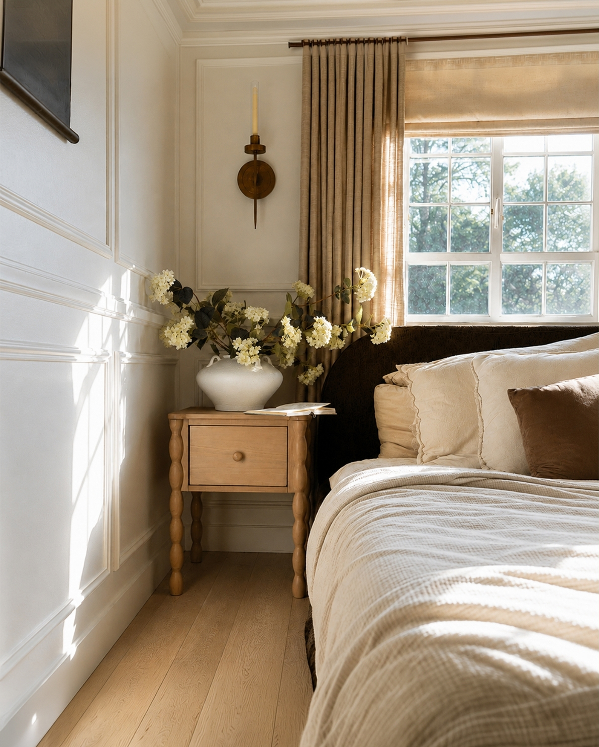 A sunlit bedroom with a wooden nightstand holding a vase of flowers next to a bed.