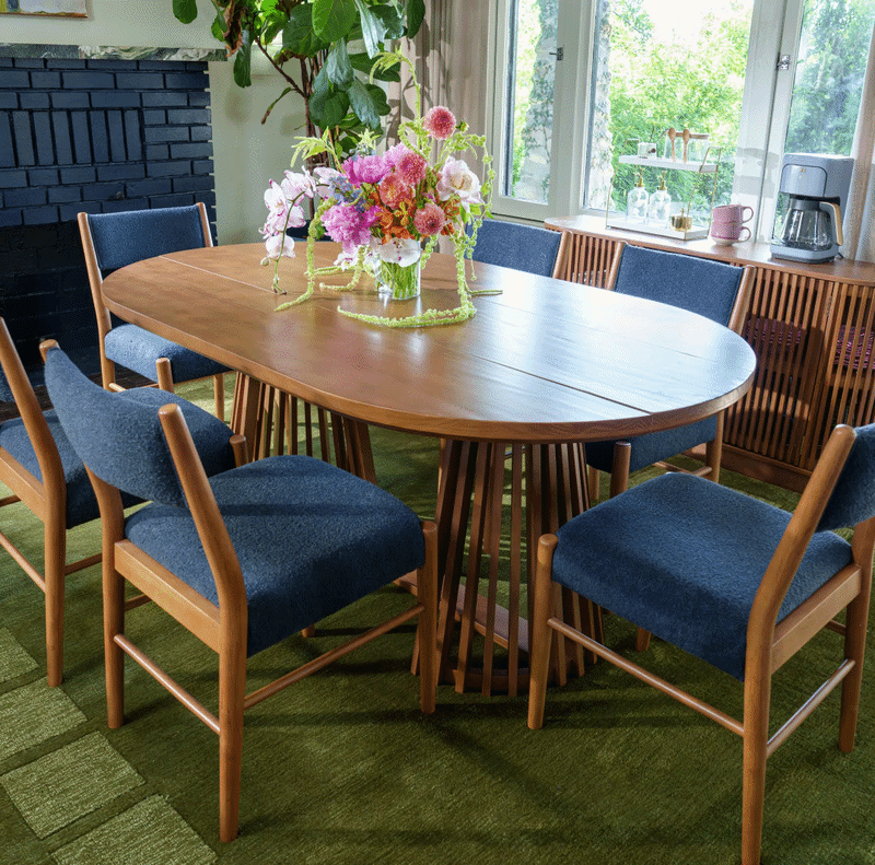 Round dining room table with navy blue upholstered chairs in natural lit dining room.