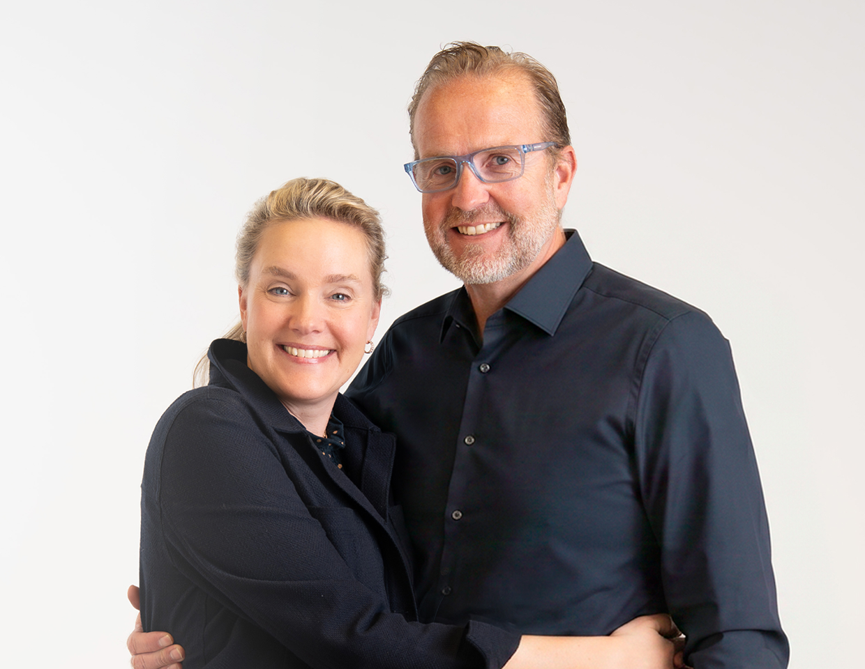 A man and woman dressed in black smiling and posing for a photo with an arm casually around each other.