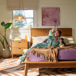Woman taking pictures of herself in her maximalist bedroom with solid wood, pecan bed frame.