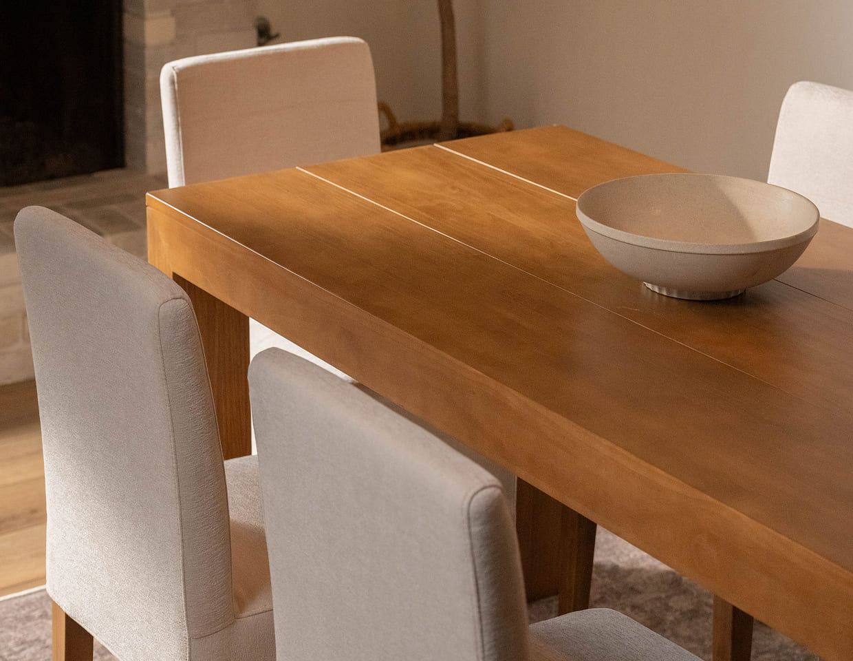 A warm wood dining table with a white bowl in the center and white upholstered dining chairs.