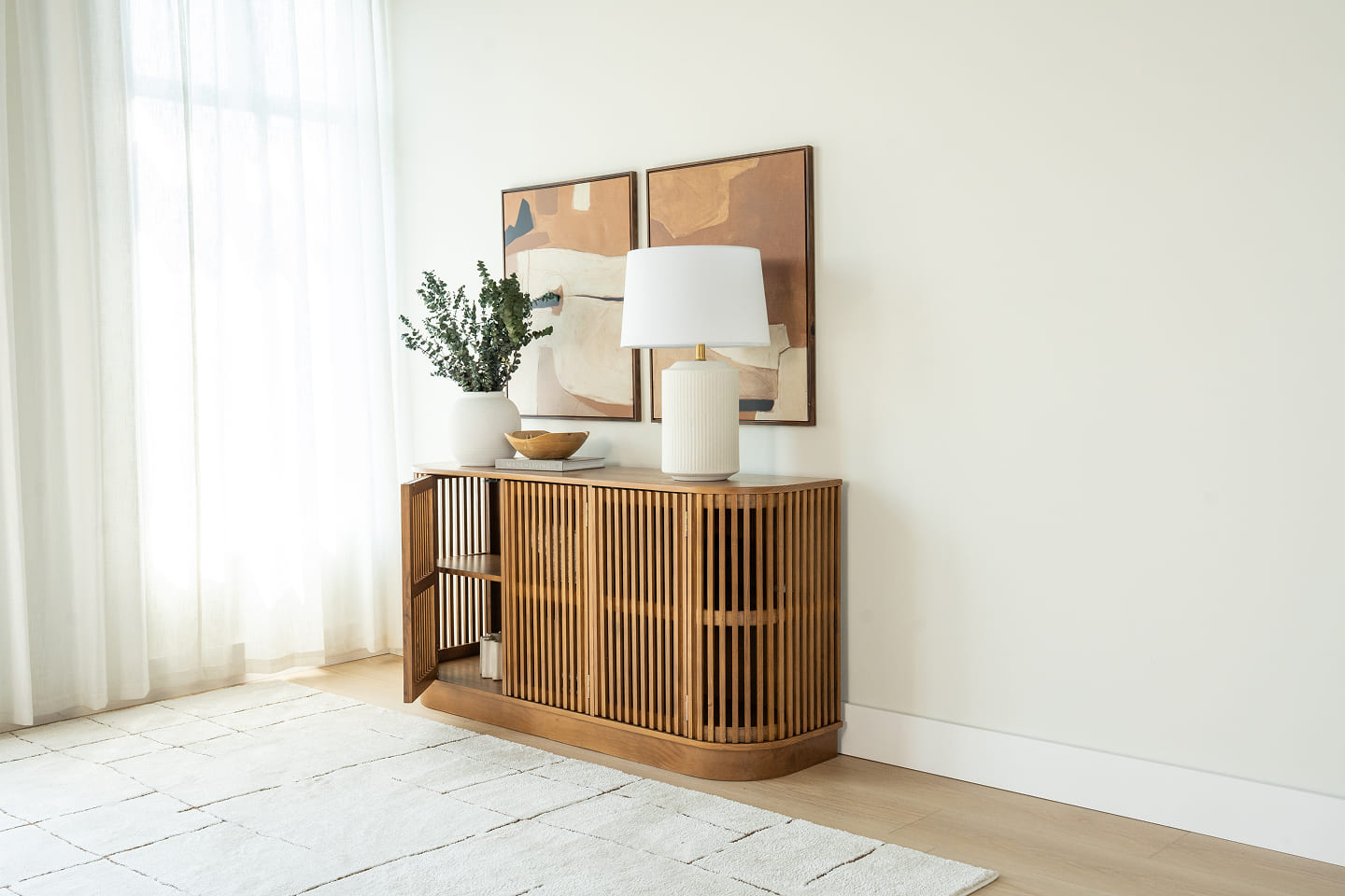 Wood sideboard with vertical slat design displaying table lamp and decorative objects below abstract artwork.