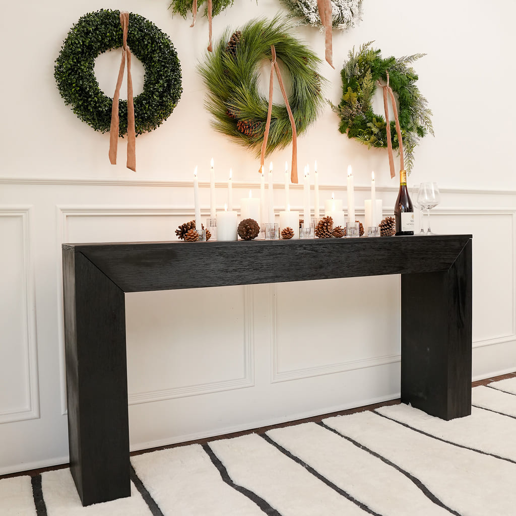 Decorative black console table with candles and wine, set against a wall with festive wreaths.