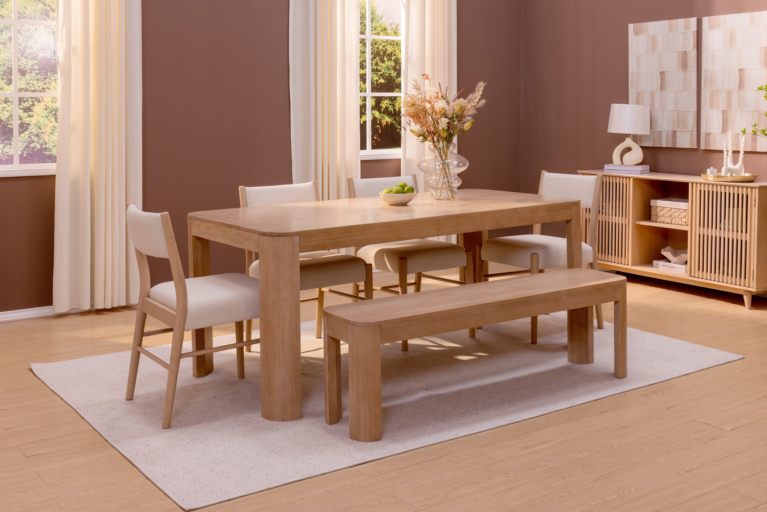 A warm dining room with light wood dining table, matching dining bench, and white upholstered dining chairs with wooden legs.