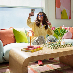 Woman taking a selfie on her maximalist, plush couch with modern, rounded corner coffee table.