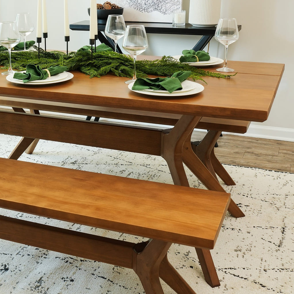 Wooden dining table set with green napkins and wine glasses on a rustic rug.