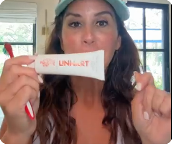 Person holding a tube labeled 'UNI HART' with a red toothbrush.