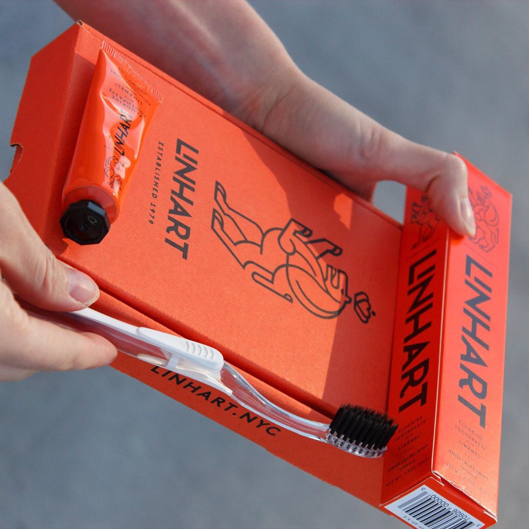 Hands holding an orange Linhart dental care set with toothbrush and toothpaste.