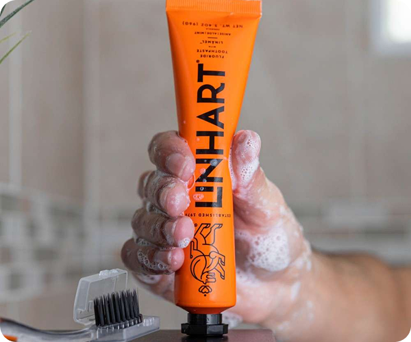 A hand holding an orange toothpaste tube with soapy bubbles, near a small brush.
