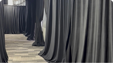Long black drapes hang in rows, creating partitions and a walkway in a large room.