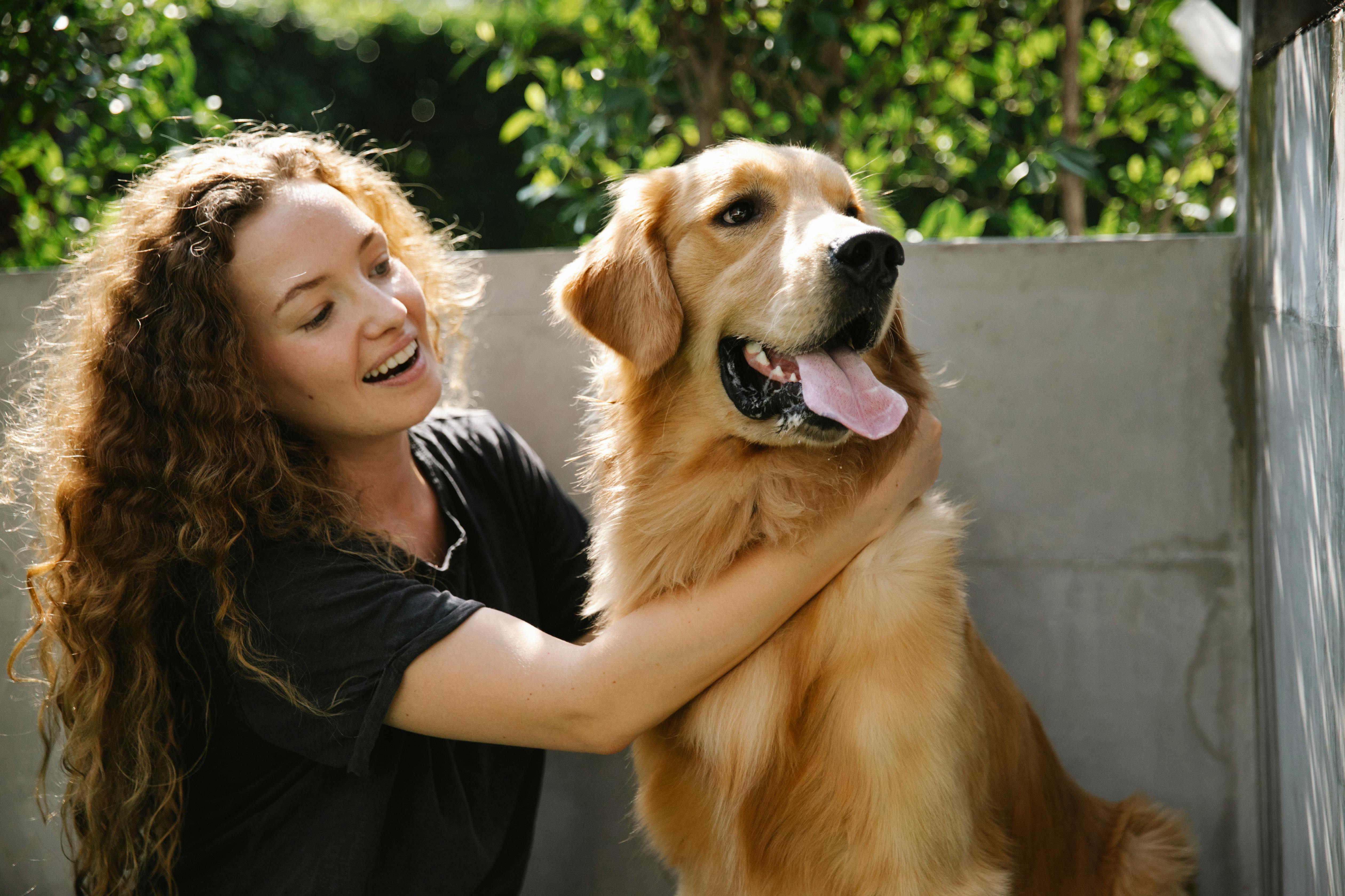 Person smiling and hugging a happy golden retriever outdoors.