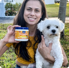 A curly-haired dog sitting with a person, next to a container labeled 'Belly Buddies.'
