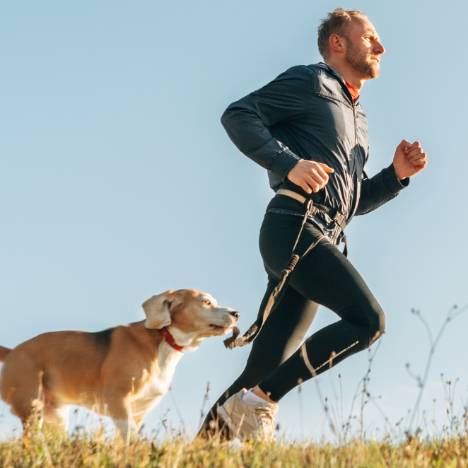 Man jogging with a dog on a grassy path under a clear sky.
