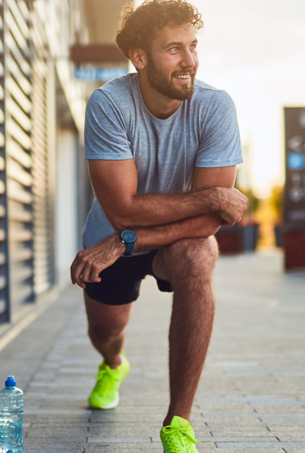 Man in workout clothes stretching outdoors, smiling.