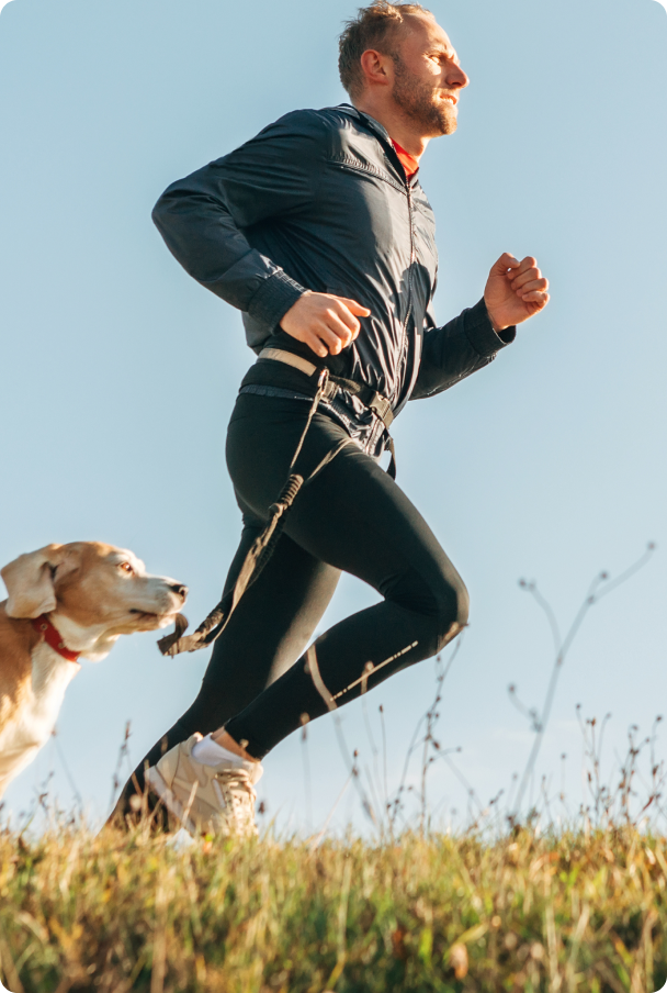 Man jogging with a dog in a grassy field under a clear sky.