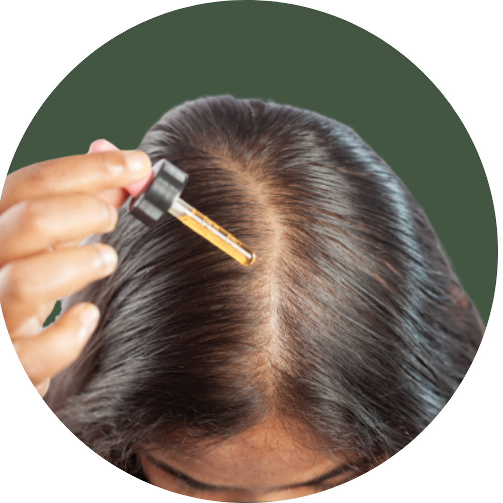 A close-up of a person applying oil to their scalp with a dropper, viewed from above.