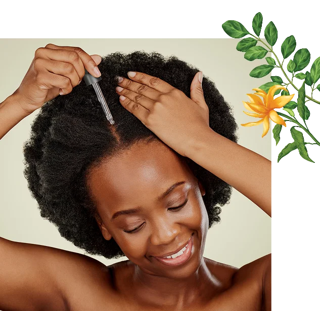 A smiling Black woman with coily hair applies a liquid to her scalp using a dropper.
