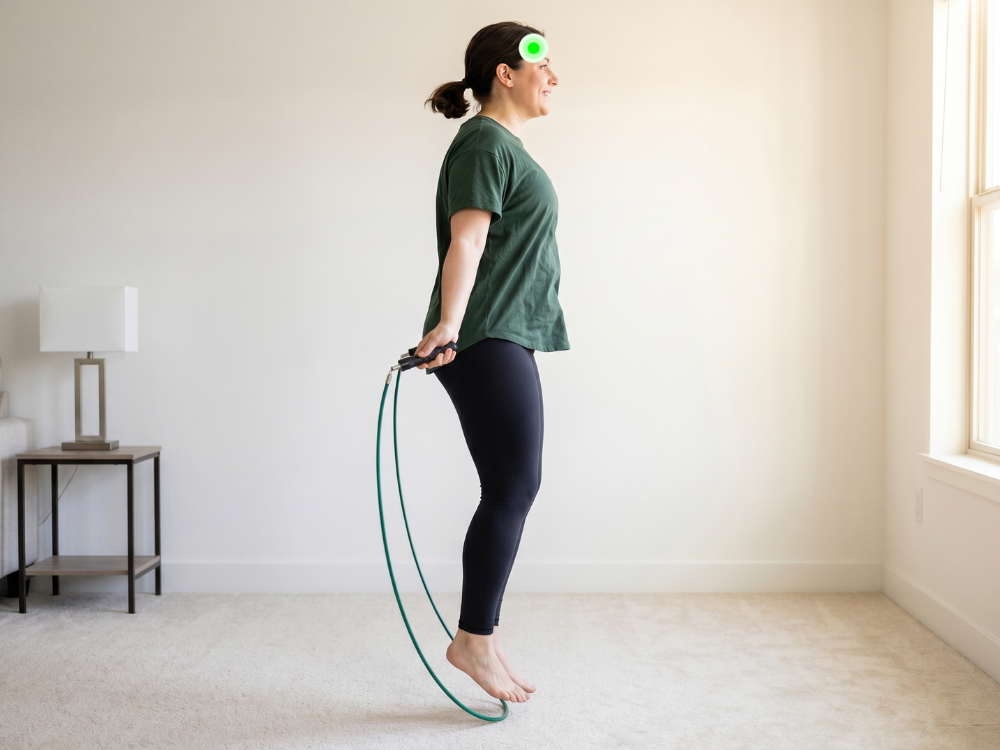 A woman in a green t-shirt and black leggings jumping rope indoors.