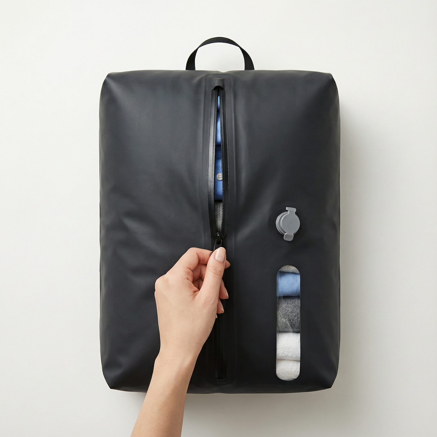 Hand opening a black travel packing bag with clothing visible inside.