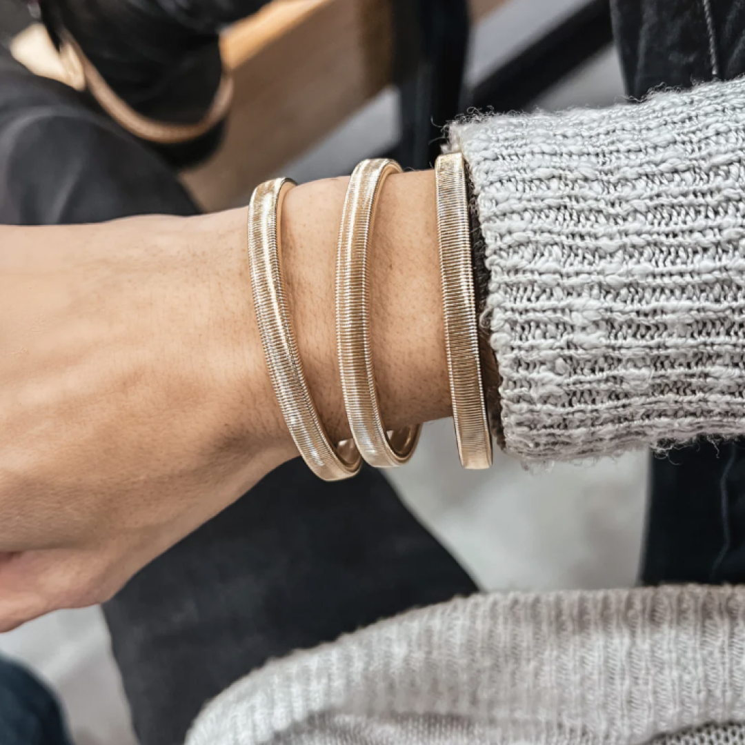 A hand wearing three gold bangles and a gray sweater.