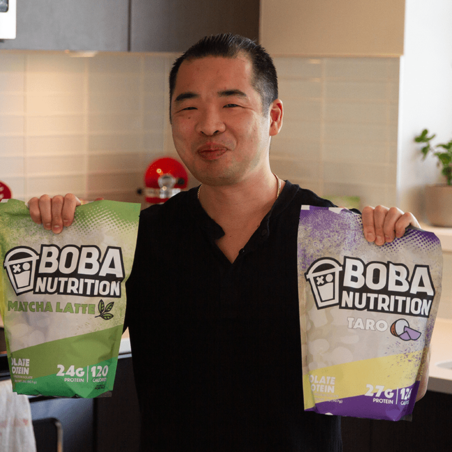 Person holding Boba Nutrition protein powder bags in a kitchen.