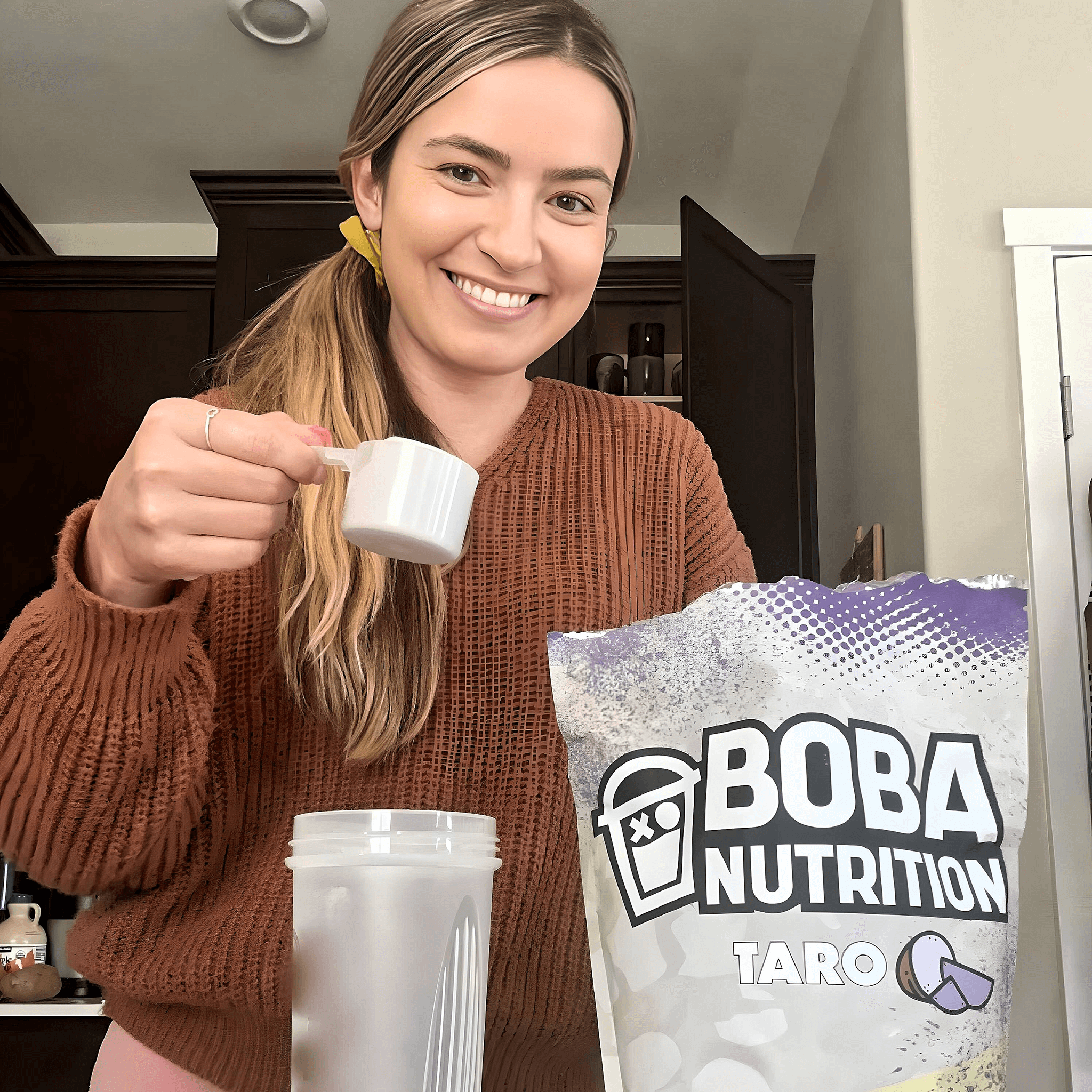 Person smiling while preparing a Boba Nutrition drink with a scoop.