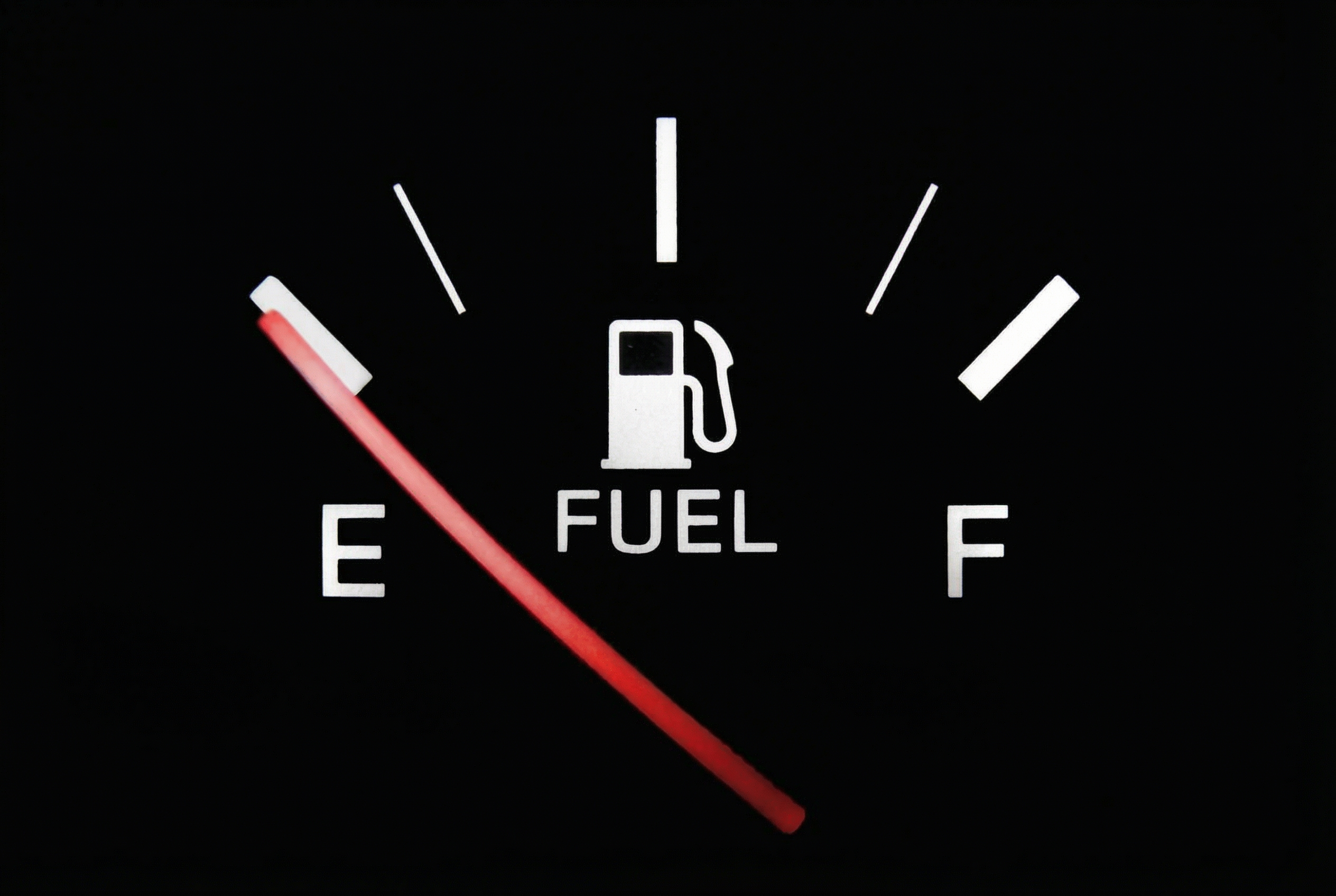 A close-up of a car's fuel gauge with the red needle pointing towards empty.