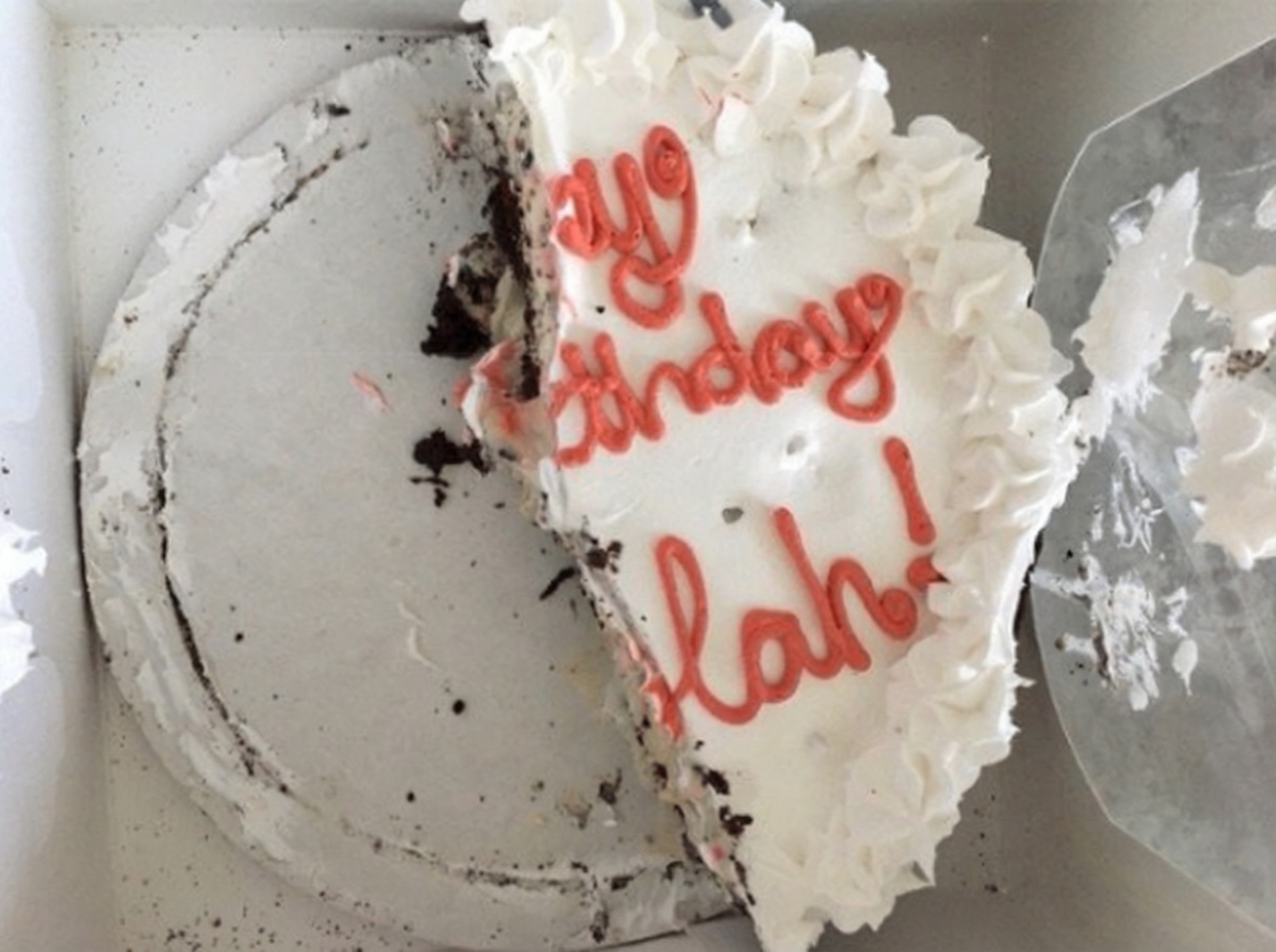 A half-eaten birthday cake with white frosting and red lettering in a cardboard box.