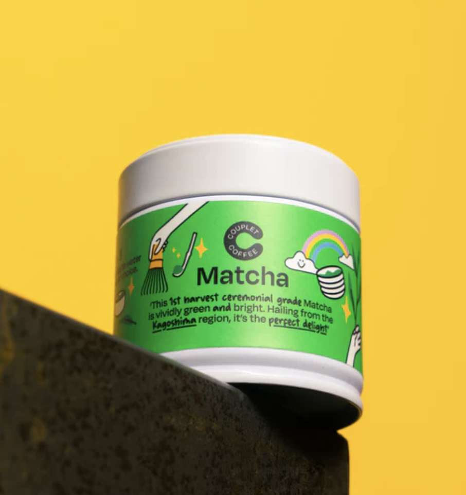 A white tin of Couplet Coffee Matcha powder sits on a dark ledge against a bright yellow background.