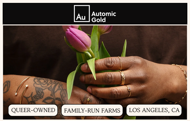 A close-up of a person's tattooed hands wearing gold rings and bracelets while holding purple tulips.