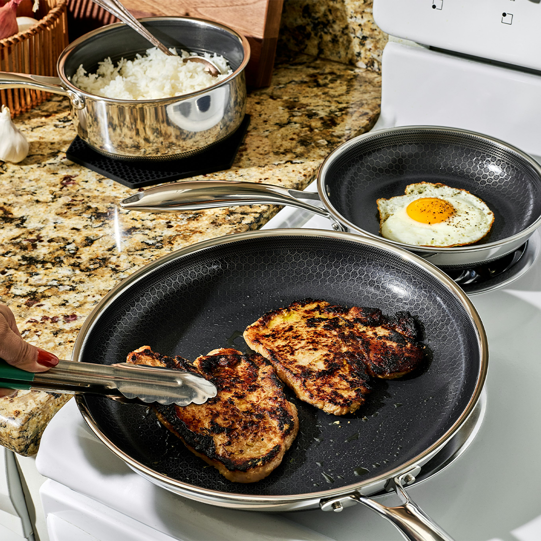 Two frying pans with cooked meat and an egg on a stove.