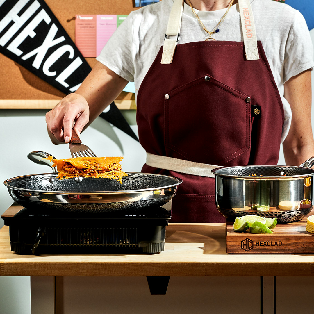 Person cooking with a spatula in a pan, wearing a maroon apron.