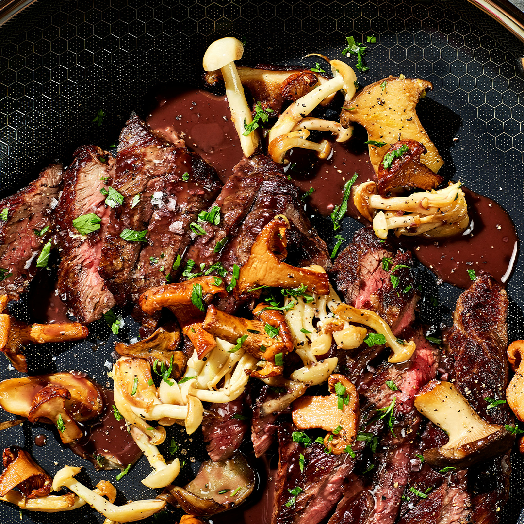 Sliced steak with mushrooms and herbs on a dark plate.